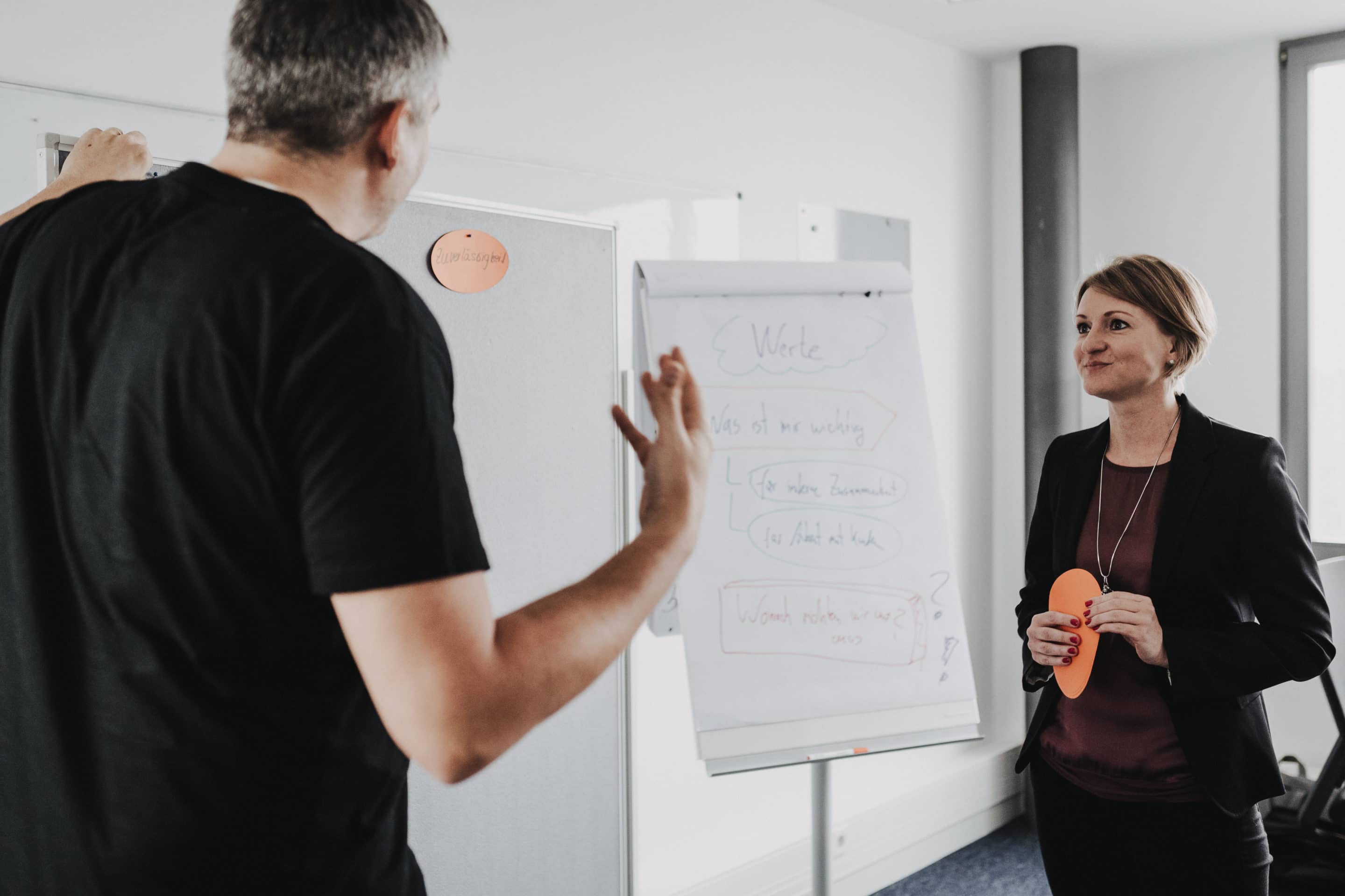 Bernd Ruffing stehend und erklärend vor einem Whiteboard mit einer Teilnehmerin